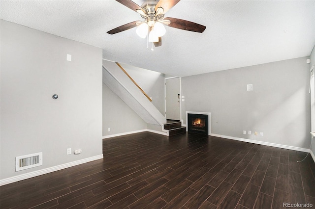 unfurnished living room featuring baseboards, wood finished floors, ceiling fan, stairs, and a lit fireplace