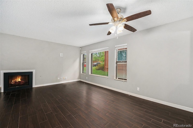 unfurnished living room featuring dark wood-style floors, ceiling fan, a lit fireplace, baseboards, and a textured ceiling