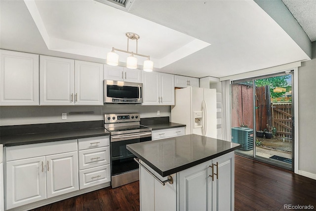 kitchen with stainless steel appliances, a tray ceiling, dark countertops, white cabinets, and dark wood finished floors
