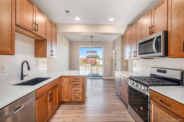 kitchen with light hardwood / wood-style floors, sink, kitchen peninsula, appliances with stainless steel finishes, and pendant lighting