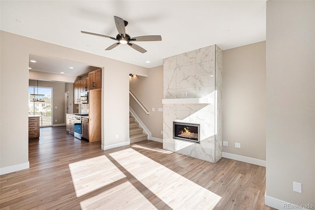 unfurnished living room with a fireplace, ceiling fan, and light wood-type flooring