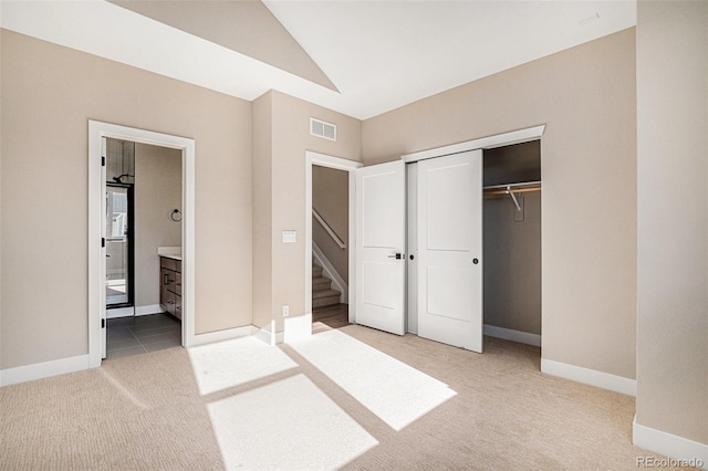 unfurnished bedroom with ensuite bathroom, light carpet, a closet, and lofted ceiling