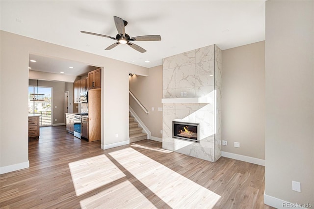 unfurnished living room with a high end fireplace, ceiling fan, and light hardwood / wood-style flooring