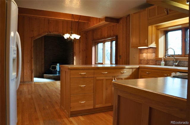 kitchen featuring white fridge with ice dispenser, a chandelier, light hardwood / wood-style flooring, sink, and wooden walls