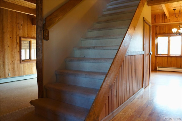 staircase featuring an inviting chandelier, a baseboard heating unit, a healthy amount of sunlight, and wood-type flooring