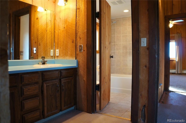 bathroom featuring tile patterned floors, wooden walls, tiled shower / bath combo, vanity, and ceiling fan