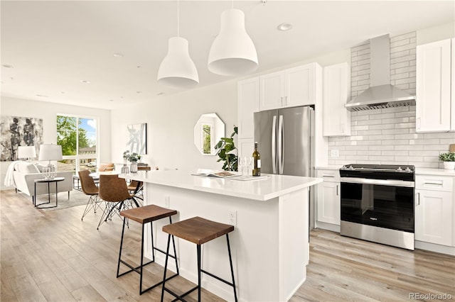 kitchen featuring appliances with stainless steel finishes, pendant lighting, white cabinetry, a kitchen island with sink, and wall chimney range hood