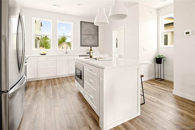 kitchen with pendant lighting, light hardwood / wood-style flooring, white cabinetry, stainless steel appliances, and a center island with sink