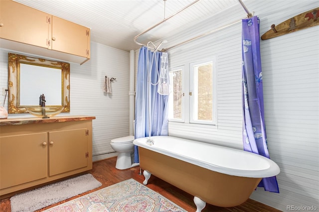 bathroom with toilet, wood finished floors, a shower with shower curtain, a freestanding bath, and vanity