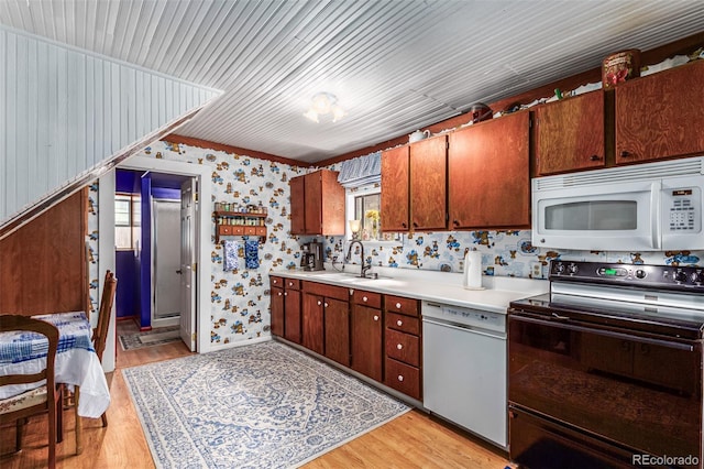 kitchen featuring wallpapered walls, light countertops, light wood-style floors, white appliances, and a sink