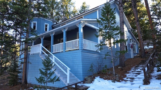 view of snow covered exterior with covered porch and stairs