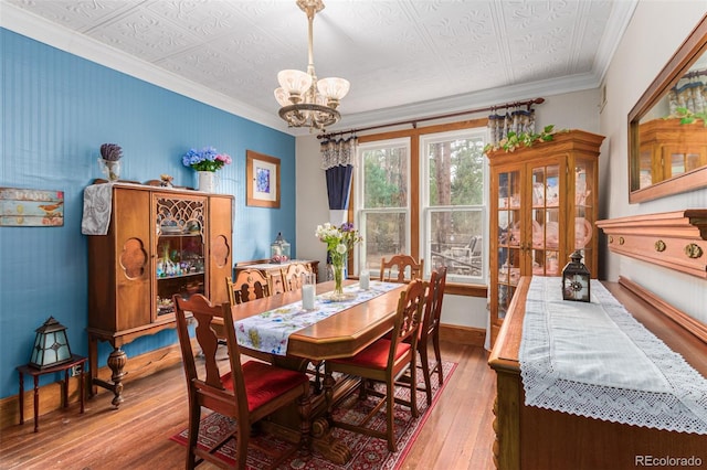 dining space featuring hardwood / wood-style flooring, an ornate ceiling, crown molding, baseboards, and a chandelier