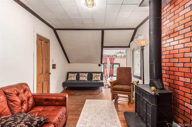 living room with vaulted ceiling, a wood stove, wood finished floors, and ornamental molding