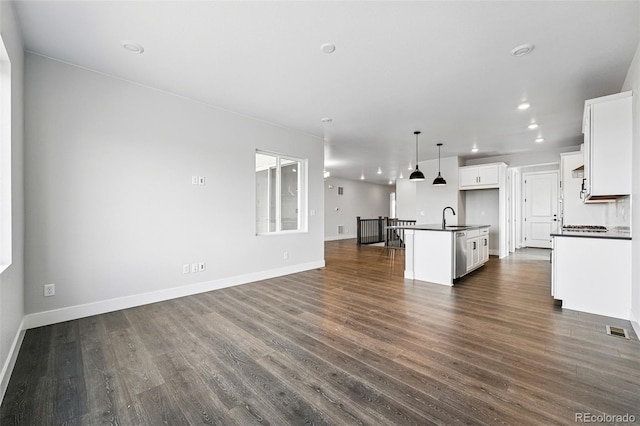 kitchen featuring dark countertops, stainless steel dishwasher, open floor plan, a kitchen island with sink, and dark wood-style flooring