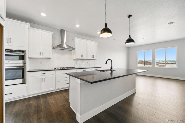 kitchen featuring wall chimney range hood, a sink, dark countertops, appliances with stainless steel finishes, and dark wood-style flooring