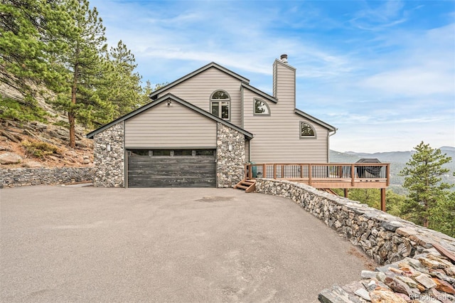 3961 Mossy Rock Ln, Evergreen, CO 80439 - view of home's exterior with driveway, a chimney, stone siding, and a wooden deck