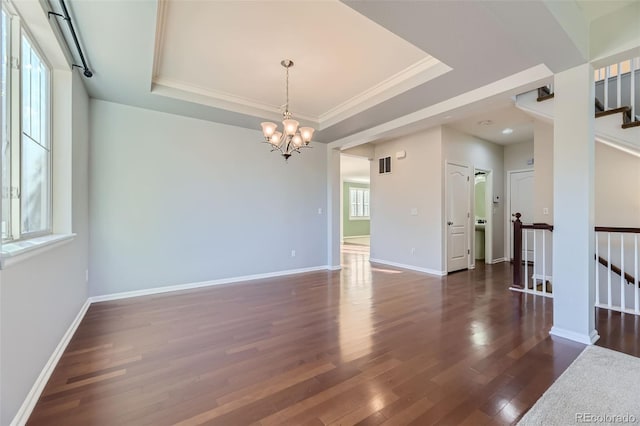 empty room with a chandelier, crown molding, dark wood-type flooring, and a tray ceiling