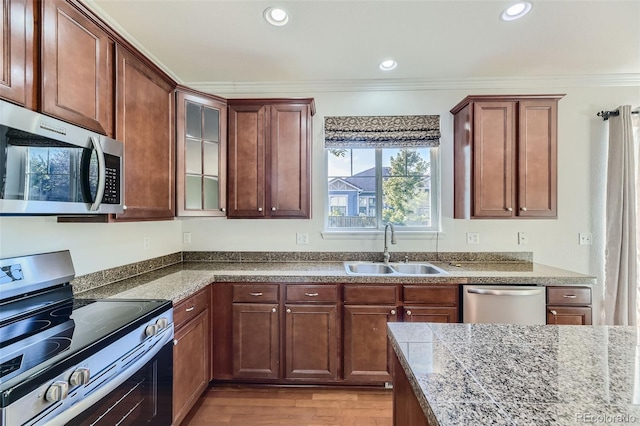 kitchen with appliances with stainless steel finishes, light wood-type flooring, ornamental molding, and sink