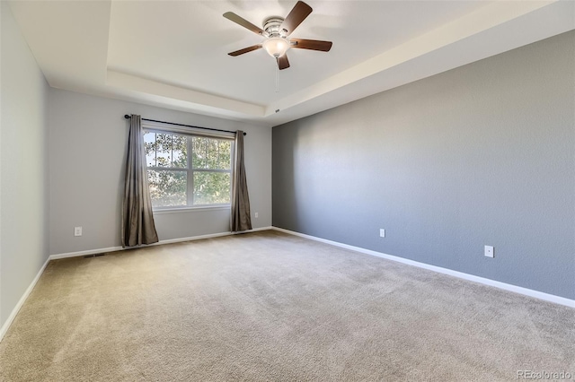 carpeted empty room with ceiling fan and a raised ceiling