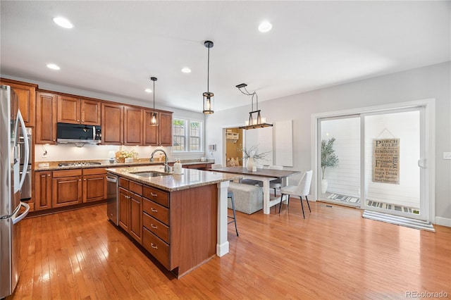 11674 Newton St, Westminster, CO 80031 - kitchen with stainless steel appliances, brown cabinetry, an island with sink, light wood-style floors, and light stone counters