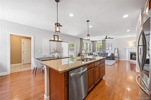 11674 Newton St, Westminster, CO 80031 - kitchen with appliances with stainless steel finishes, brown cabinetry, light wood-type flooring, a kitchen island with sink, and a tile fireplace