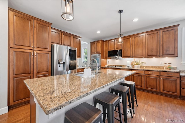11674 Newton St, Westminster, CO 80031 - kitchen with stainless steel appliances, brown cabinets, light wood-style floors, light stone counters, and recessed lighting