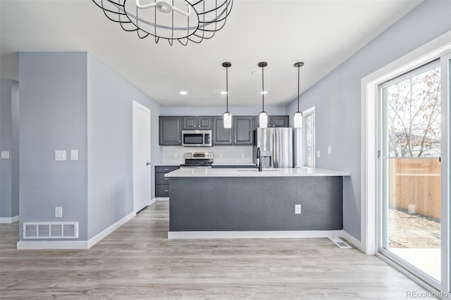 kitchen with appliances with stainless steel finishes, gray cabinetry, hanging light fixtures, a notable chandelier, and light hardwood / wood-style flooring