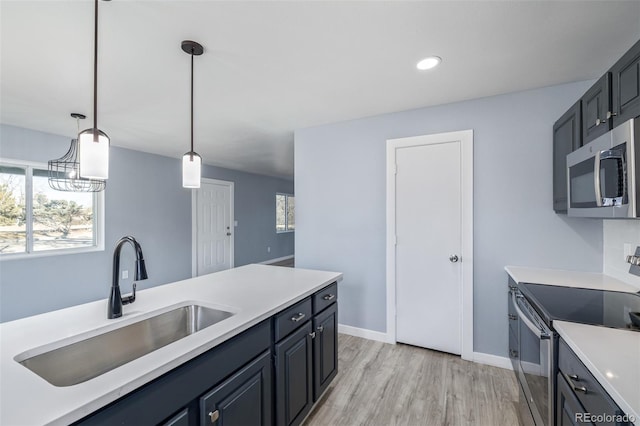 kitchen with stainless steel appliances, sink, pendant lighting, and light wood-type flooring