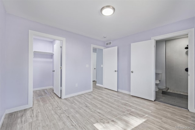 unfurnished bedroom featuring a spacious closet, connected bathroom, a closet, and light wood-type flooring