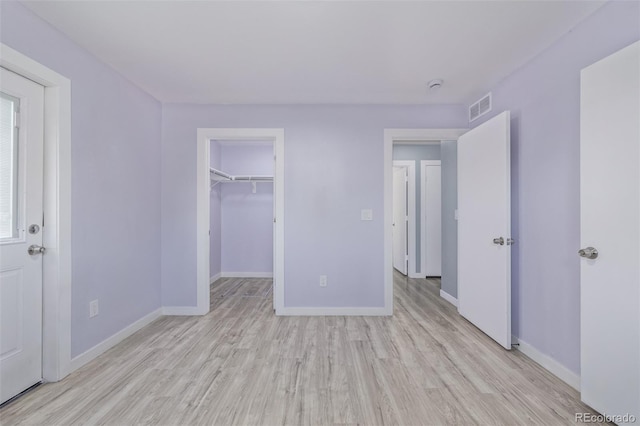 unfurnished bedroom featuring a spacious closet, a closet, and light wood-type flooring