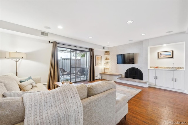 living room featuring dark wood-type flooring, a brick fireplace, and a baseboard heating unit