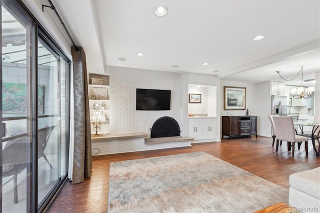 living room with dark wood-type flooring, a chandelier, and a brick fireplace