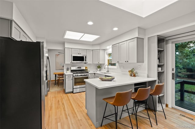 3458 S Norfolk Way, Aurora, CO 80013 - kitchen featuring stainless steel appliances, a peninsula, gray cabinetry, light wood-style flooring, and recessed lighting