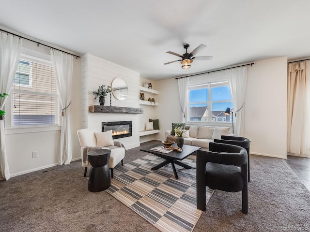 living room with ceiling fan, a large fireplace, and dark colored carpet