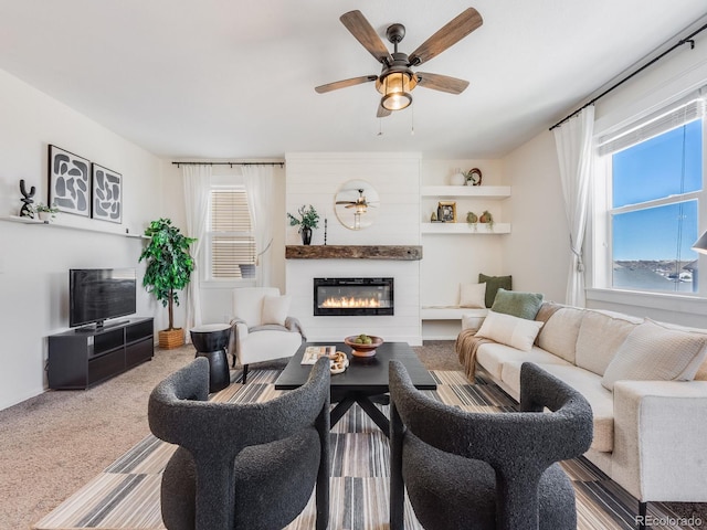 carpeted living room with ceiling fan and a large fireplace