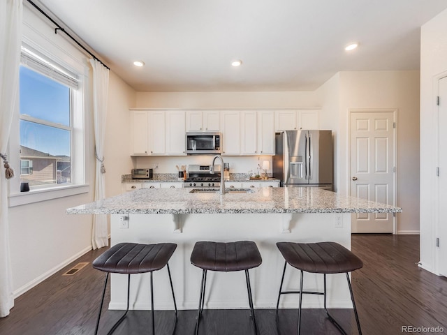 kitchen featuring white cabinets, appliances with stainless steel finishes, sink, light stone counters, and a center island with sink