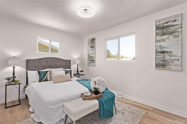 bedroom featuring multiple windows, light wood-style flooring, and baseboards