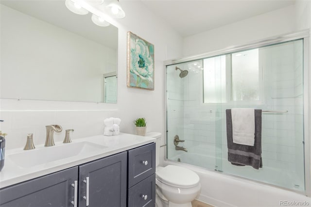bathroom featuring toilet, vanity, decorative backsplash, and bath / shower combo with glass door