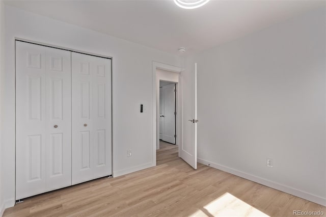 unfurnished bedroom featuring light wood-type flooring, baseboards, and a closet
