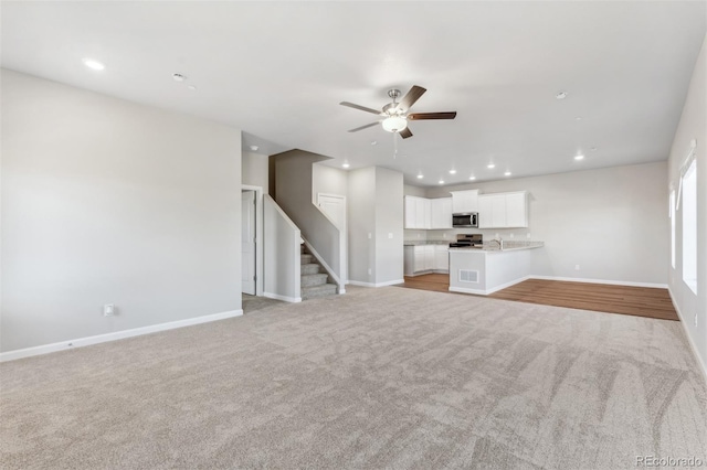 unfurnished living room featuring light carpet, sink, and ceiling fan