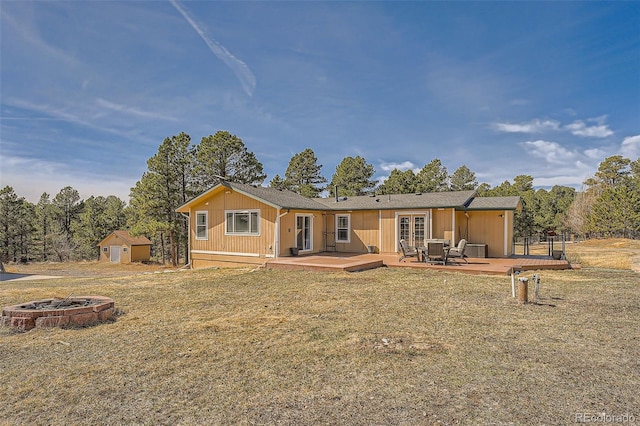 rear view of property featuring an outdoor structure, a storage unit, french doors, a fire pit, and a deck