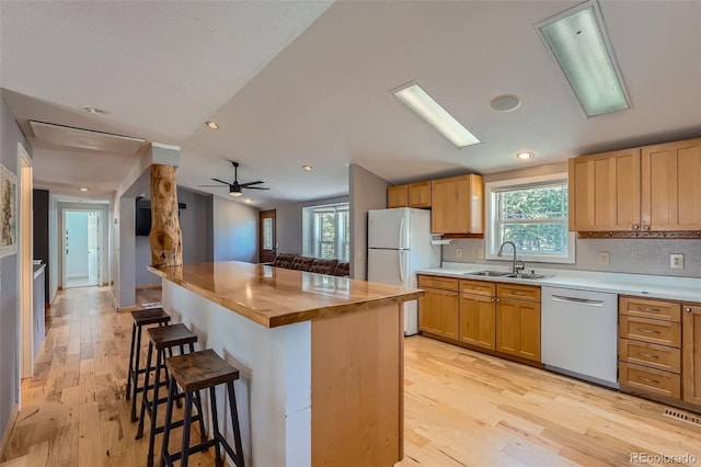 kitchen featuring white appliances, a breakfast bar area, wooden counters, a sink, and light wood-style floors