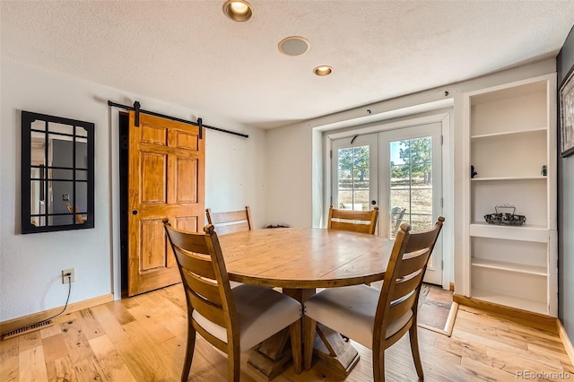 dining room featuring a barn door, light wood-style flooring, baseboards, and a textured ceiling