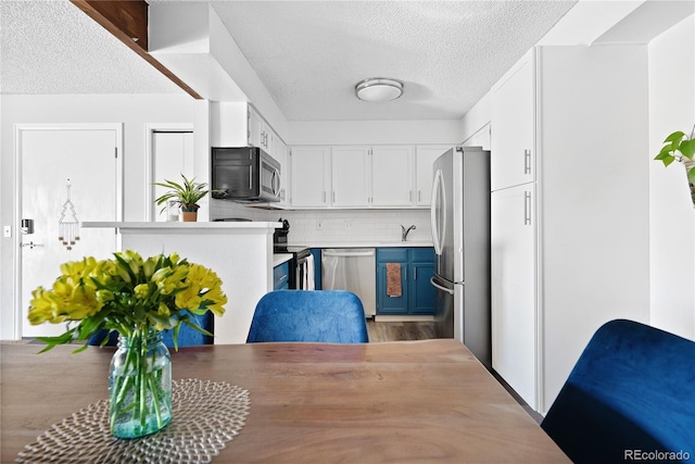 209 Wright St Unit 204, Lakewood, CO 80228 - kitchen with blue cabinetry, backsplash, stainless steel appliances, a textured ceiling, and white cabinetry