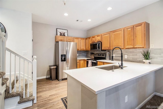 kitchen with sink, appliances with stainless steel finishes, tasteful backsplash, light hardwood / wood-style floors, and kitchen peninsula