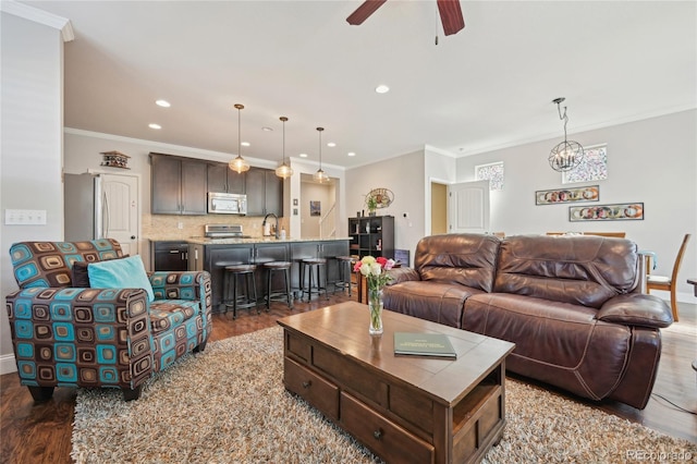 living room with crown molding, wood-type flooring, ceiling fan with notable chandelier, and sink