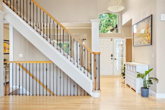 entrance foyer with a towering ceiling, a notable chandelier, hardwood / wood-style floors, and ornate columns