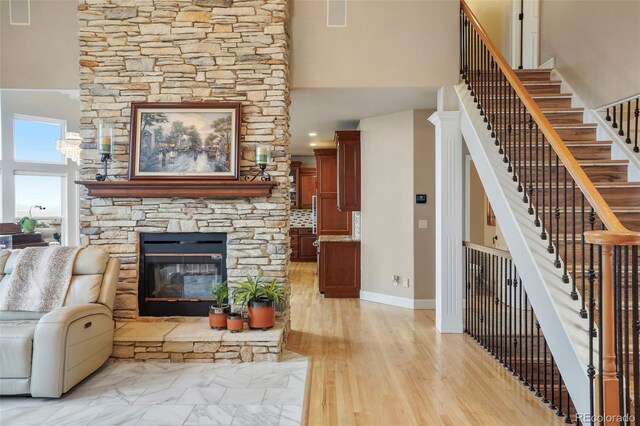 living room featuring a towering ceiling, a stone fireplace, and light wood-type flooring