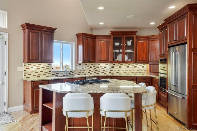 kitchen featuring sink, light wood-type flooring, a kitchen island, backsplash, and stainless steel appliances