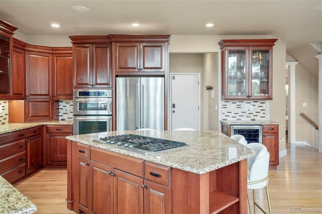 kitchen with light stone counters, stainless steel appliances, light wood-type flooring, and backsplash